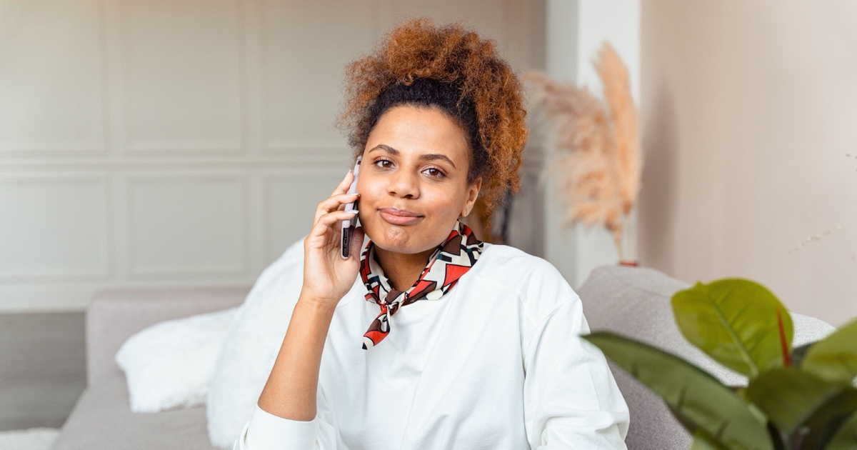 Woman smiling while talking on the phone, sitting on a couch at home